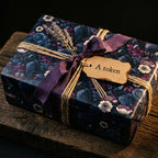 Luxury dark floral wrapping paper with crows on a gift box, styled with purple ribbon and a rustic tag by Wrapped Studios.