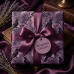 Elegant raven gift wrap with dark purple ribbon bow on a square present, against matching draped fabric background.