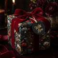 Luxury dark floral wrapping paper with a burgundy velvet ribbon and "With Love" tag by Wrapped Studios.