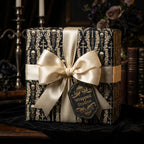 Gothic skull wrapping paper in black and gold with a luxury satin bow on a gift box by Wrapped Studios.