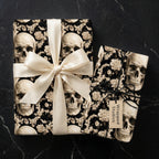 Gothic skull wrapping paper with cream floral pattern and elegant satin bow by Wrapped Studios.