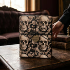 Gothic skull wrapping paper by Wrapped Studios on a gift box tied with black twine on a rustic wood table.