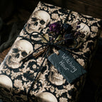 Gothic skull wrapping paper by Wrapped Studios with dried roses and a Witching Hour tag on a gift.