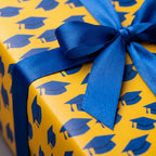 Yellow and blue graduation wrapping paper with mortarboard pattern and satin bow by Wrapped Studios.