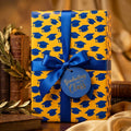 Yellow and blue graduation wrapping paper with graduation caps, satin bow, and gift tag by Wrapped Studios.