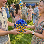 Yellow graduation wrapping paper with blue caps on a gift held by a couple, by Wrapped Studios.