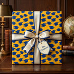 Yellow and blue graduation wrapping paper with mortarboards and a cream satin bow by Wrapped Studios.