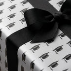Graduation wrapping paper with black mortarboard caps and a black grosgrain bow by Wrapped Studios.