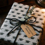 Graduation wrapping paper with black mortarboard cap pattern and twine by Wrapped Studios.