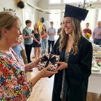 Graduate receives a gift in pink graduation wrapping paper with a black bow, by Wrapped Studios.