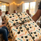 Graduation wrapping paper with caps and diplomas tied with twine on a gift box by Wrapped Studios.
