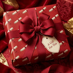 Red scroll pattern luxury gift wrap with a large ribbon bow and gift tag, by Wrapped Studios.