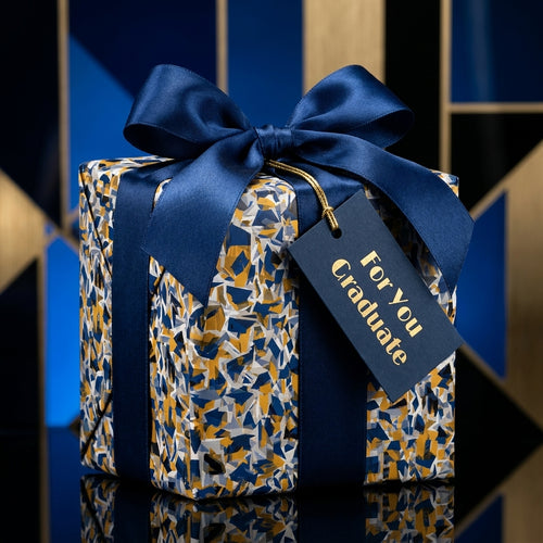 Luxury graduation gift wrapped in abstract blue and gold paper with a navy satin bow and "For You Graduate" tag.