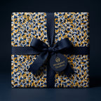 Luxury gift wrapped in modern geometric paper with navy, gold, and white shards, finished with a navy ribbon by Wrapped Studios.