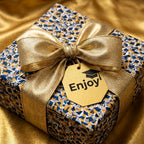 Luxury graduation gift box with blue and gold patterned wrapping paper, a satin gold ribbon, and an "Enjoy" gift tag.