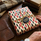 Graduation wrapping paper with red and black graduate pattern and gold cord bow, by Wrapped Studios.