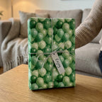 Playful green balloon birthday wrapping paper on a gift with a silver string, by Wrapped Studios.