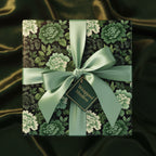 Elegant square gift wrapped in dark floral wrapping paper with a satin green ribbon and bow.