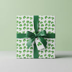 Square gift wrapped in shamrock St. Patrick's Day wrapping paper with a green satin bow and tag.