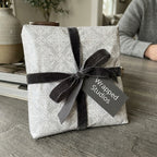 Elegant floral wrapping paper in grey with a dark velvet ribbon and a Wrapped Studios gift tag.