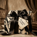 Gothic wrapping paper with skulls and ravens, tied with a luxury black satin bow by Wrapped Studios.