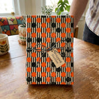 Retro orange and black polka dot striped wrapping paper on a gift with twine, by Wrapped Studios.