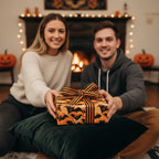 Couple exchanging a Halloween gift wrapped in orange and black bat wrapping paper with striped ribbon.
