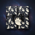 Wrapped gift box with black satin ribbon and ghost pattern Halloween wrapping paper.