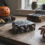 Wrapped Halloween gift with silver string and ghost-patterned gift wrap on a wooden table.