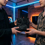 People exchanging a gift wrapped in modern black paper with a subtle branch design and a matching ribbon.