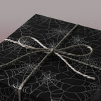 Black Halloween gift wrap with spiderweb pattern and rustic twine bow.
