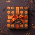 Square Halloween gift wrapped in pumpkin wrapping paper with an orange satin bow.