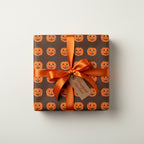 Square gift wrapped in brown Halloween wrapping paper with jack-o'-lanterns and tied with an orange ribbon.