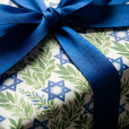 Hanukkah wrapping paper with Star of David & olive leaves, tied with blue satin ribbon by Wrapped Studios.