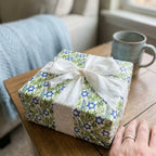 Hanukkah wrapping paper with blue Stars of David, green leaves, and a white ribbon by Wrapped Studios.