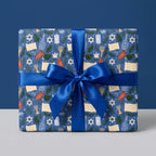 Hanukkah wrapping paper with menorahs and Stars of David, tied with a blue ribbon by Wrapped Studios.