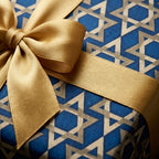 Luxury Hanukkah gift wrap with blue Star of David pattern and a gold satin bow, by Wrapped Studios.