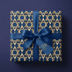 Elegant Hanukkah gift wrap with gold Star of David pattern and blue bow by Wrapped Studios.