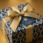 Luxury Hanukkah wrapping paper in blue and gold Star of David pattern with gold ribbon by Wrapped Studios.