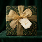 Elegant gift box wrapped in dark green holly-themed Christmas wrapping paper and gold ribbon.