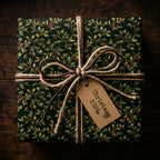 Dark green Christmas gift wrap with holly berry pattern, tied with twine and leather ribbon.