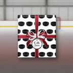 Hockey puck wrapping paper with a red and white ribbon, gift tag, and ice rink background.