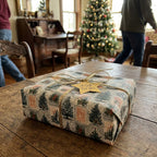 Vintage Christmas wrapping paper with tree pattern and gold bow on a rustic table by Wrapped Studios.