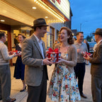 Couple exchanging gifts in red retro wrapping paper outside a vintage theater by Wrapped Studios.