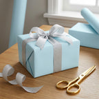 Light ice blue gift box with silver ribbon and gold scissors on a wooden surface. Ice blue wrapping paper solid color.