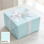 Light blue wrapping paper on a square gift box tied with a white grosgrain ribbon.