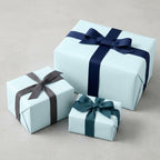 Three light blue gift boxes wrapped in solid color wrapping paper and dark blue, grey, and teal ribbons.