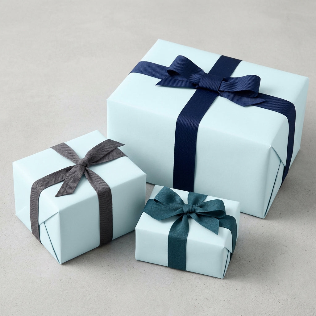 Three light blue gift boxes wrapped in solid color wrapping paper and dark blue, grey, and teal ribbons.