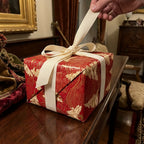 Hand untying cream ribbon on luxury red and gold Christmas wrapping paper by Wrapped Studios.