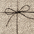 Close-up of a gift wrapped in cream paper with a brown abstract pattern, tied with a simple brown string bow.